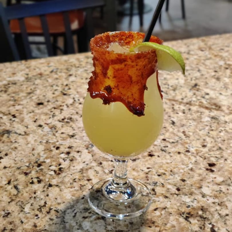 A Mexican margarita with a chili-lime rim and a lime wedge on a speckled countertop.