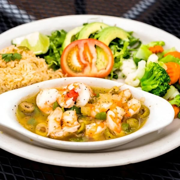 Mexican shrimp dish with rice, mixed vegetables, avocado, and a tomato slice on a white plate.