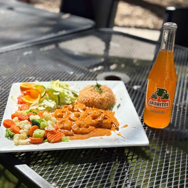 Shrimp in red sauce with rice, vegetables, and a Jarritos Mandarin soda on an outdoor table.