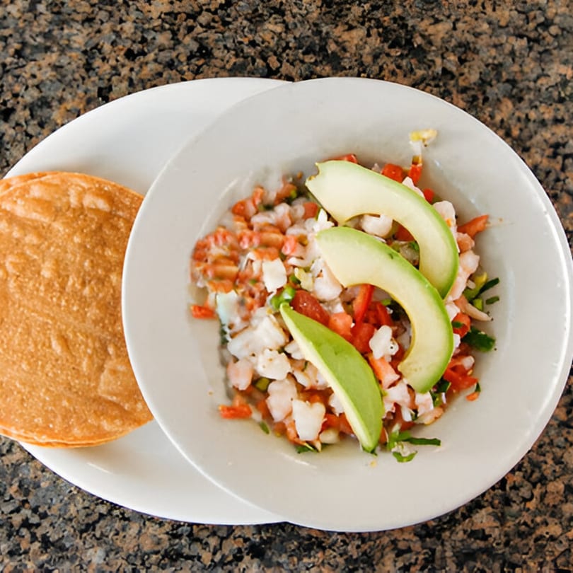 Mexican shrimp ceviche with avocado slices and a side of tostadas on a white plate.