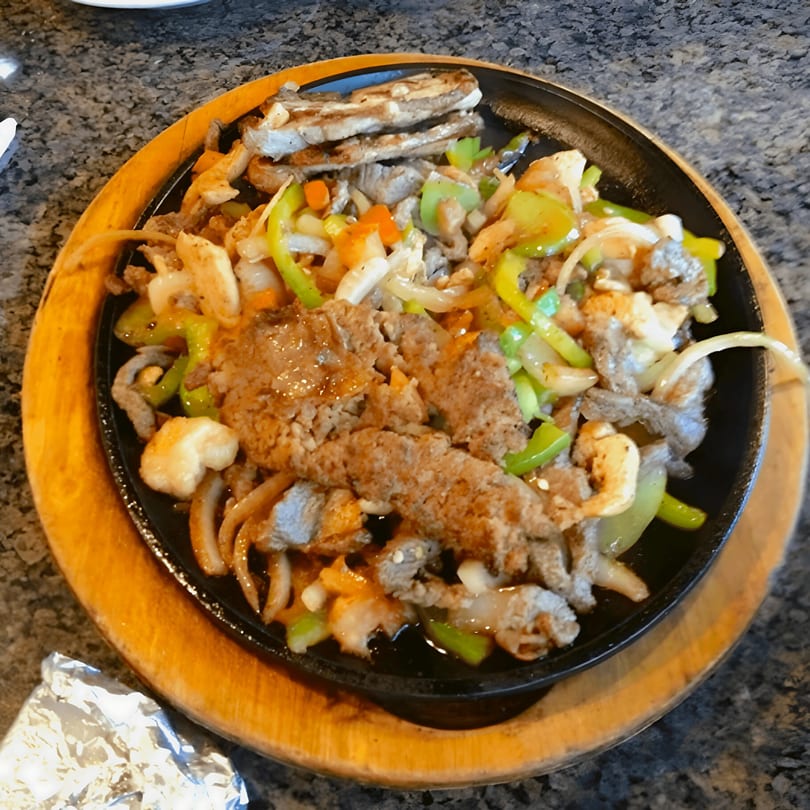 Sizzling fajitas with steak, shrimp, onions, and bell peppers on a cast iron skillet.