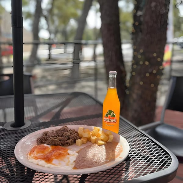 Mexican breakfast plate with eggs, beans, potatoes, and a Jarritos soda on an outdoor patio table.