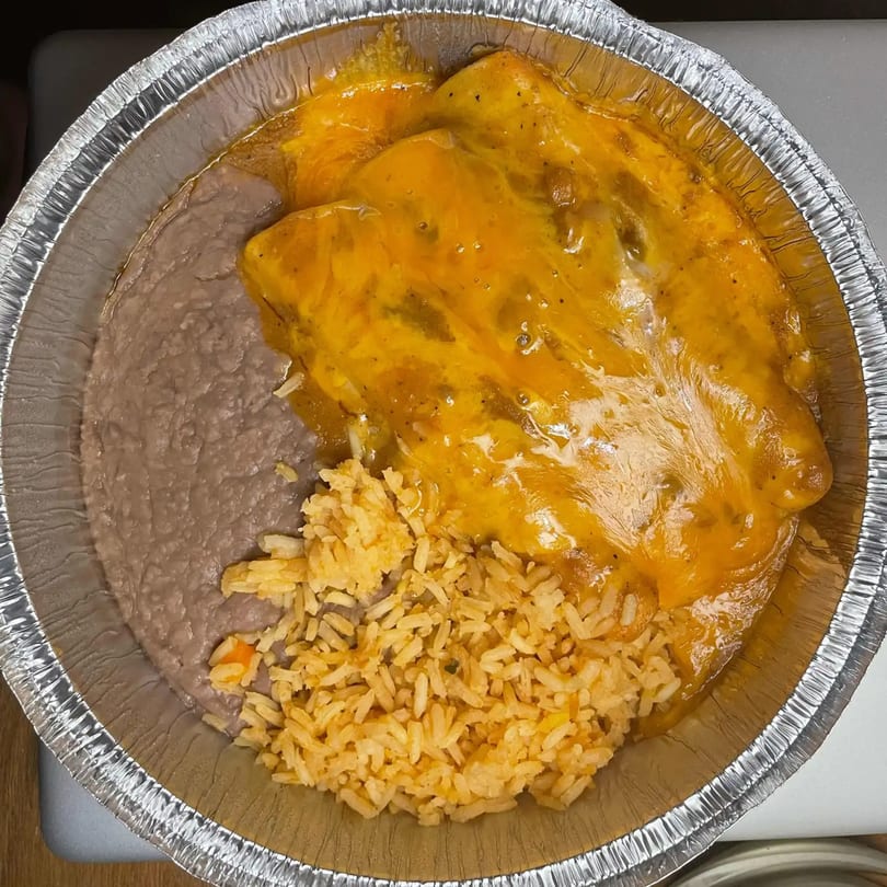 Mexican enchiladas with melted cheese, refried beans, and rice in a foil takeout container.