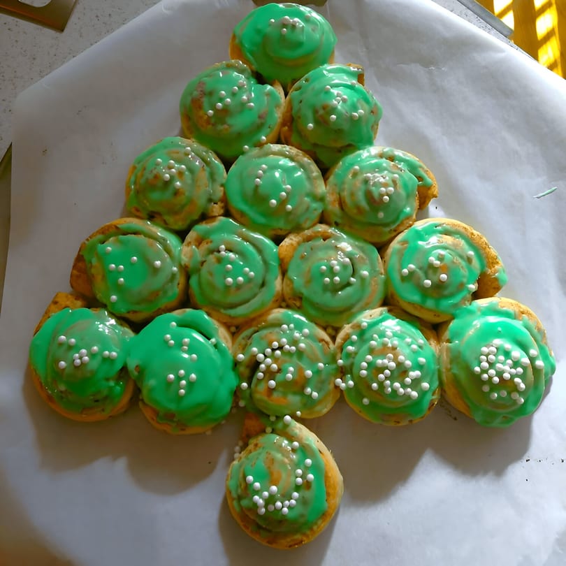 A Christmas tree-shaped arrangement of cinnamon rolls with green icing and white sprinkles.